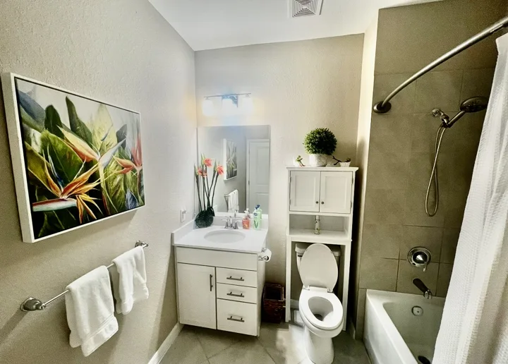 Bathroom with tropical artwork, white storage, and layered towels