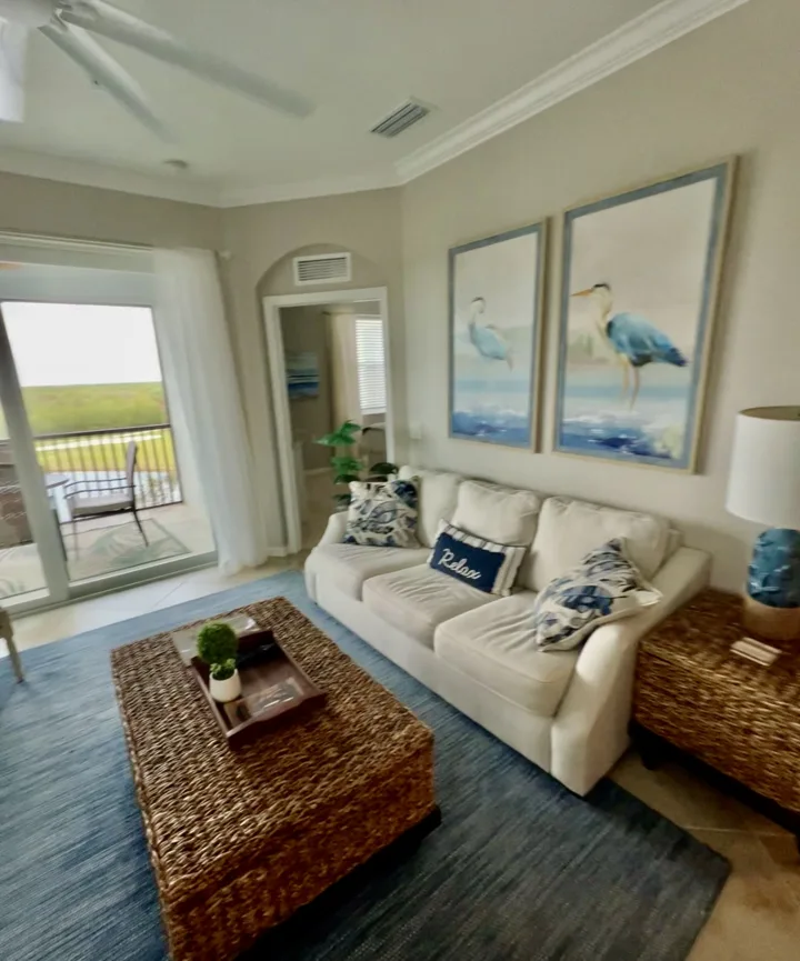 Living room with a white sofa, woven coffee table, and coastal artwork