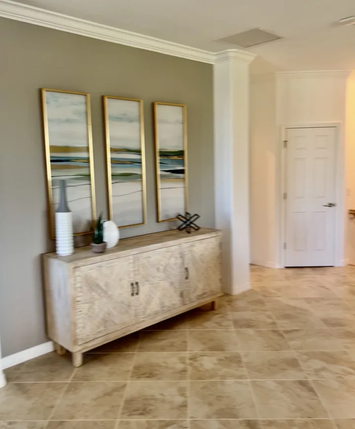 Light wood entry console below three tall framed artworks