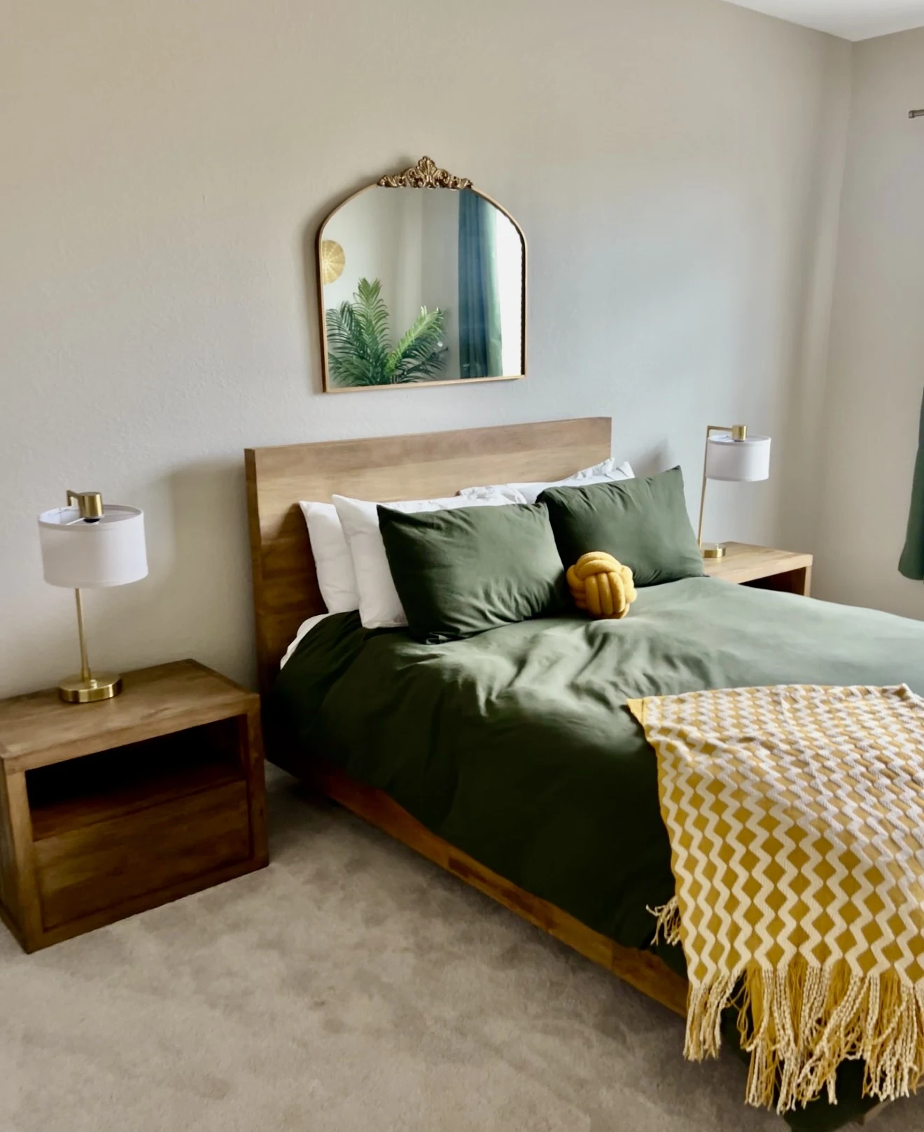 Bedroom with green bedding, warm wood furnishings, brass lamps, and mustard accents