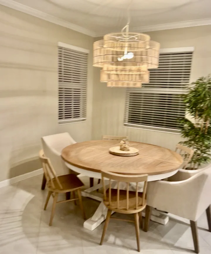 Round wood dining table with upholstered chairs and a woven pendant