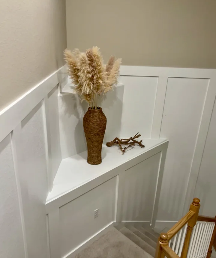 Stair landing with white wall paneling, a woven vase, and dried grasses