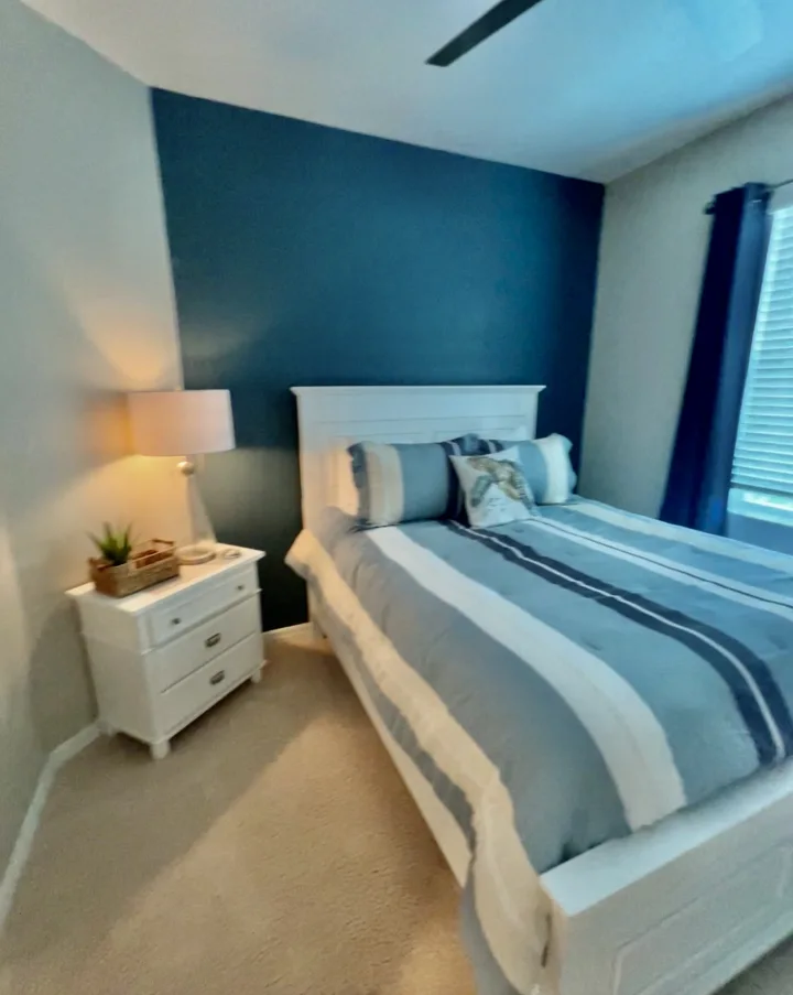 Bedroom with a blue accent wall, striped bedding, and a white bedside chest